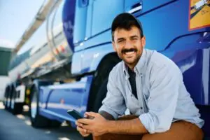 A happy truck driver using a cell phone in the parking lot of a truck stop health clinic