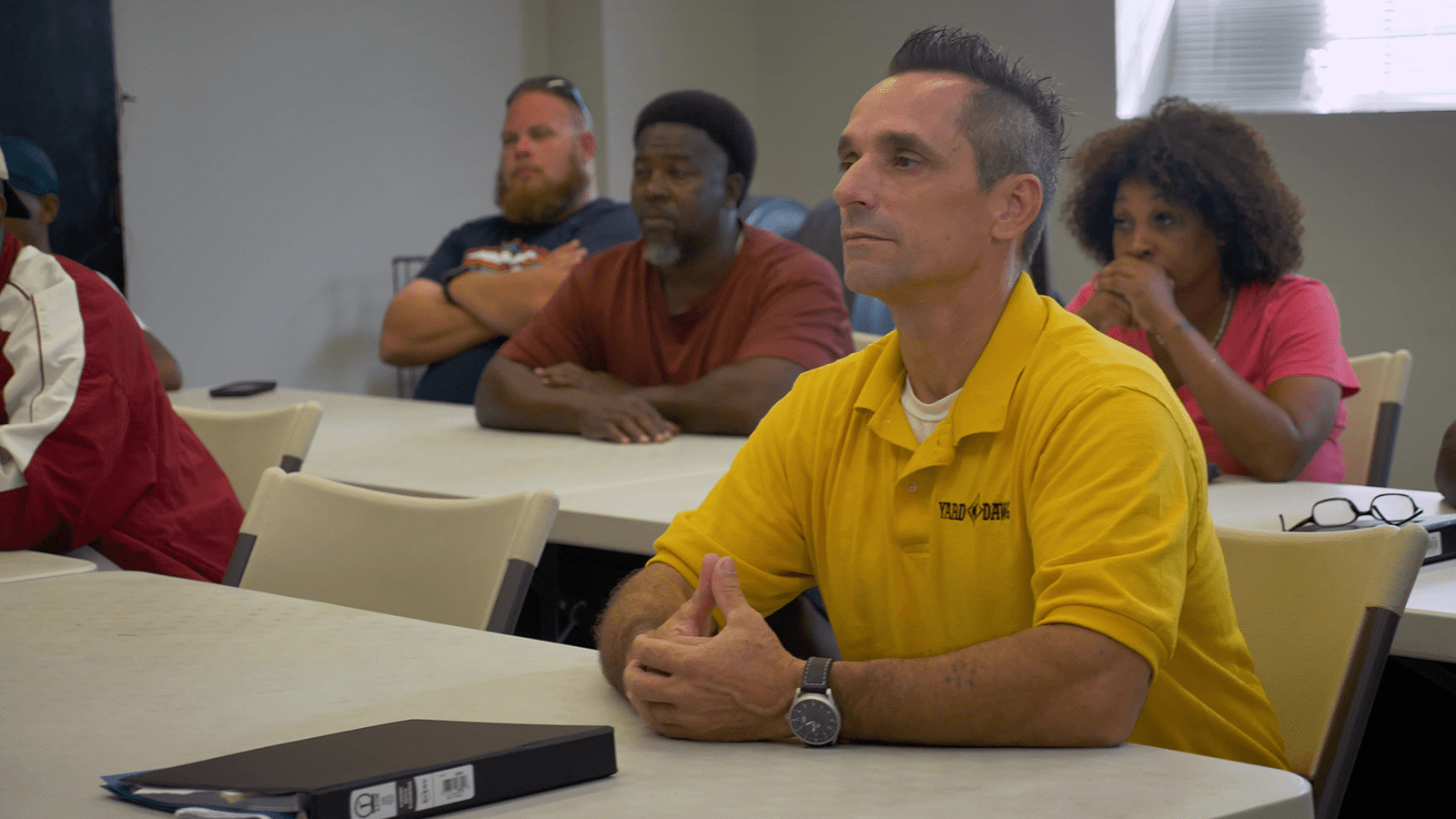 A man in a yellow shirt sits in a classroom with other students taking a CDL class.