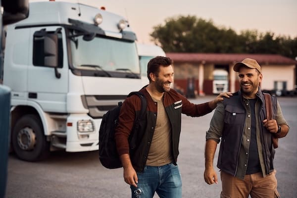 Two cheerful truck drivers having fun in a parking lot before their weekday training, as opposed to feeling frustrated and lost at weekend CDL schools