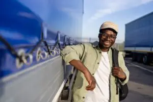 A man with a good truck driver work life balance smiles while leaning against his truck
