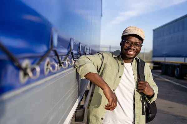 A man with a good truck driver work life balance smiles while leaning against his truck