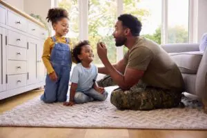 A trucking dad sitting on the floor with a puzzle piece in his hand as he helps his two daughters work on a puzzle together
